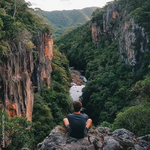 Man on rock above canyon with river, green trees on rocky walls