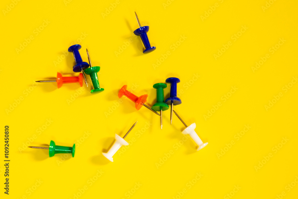 Top view of multicolored thumbtacks scattered on a yellow background, concept of objects and work materials