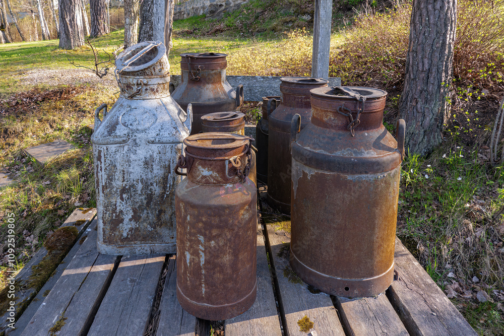 A collection of weathered milk cans rests on a rustic wooden platform, A collection of weathered milk cans rests on a rustic wooden platform,