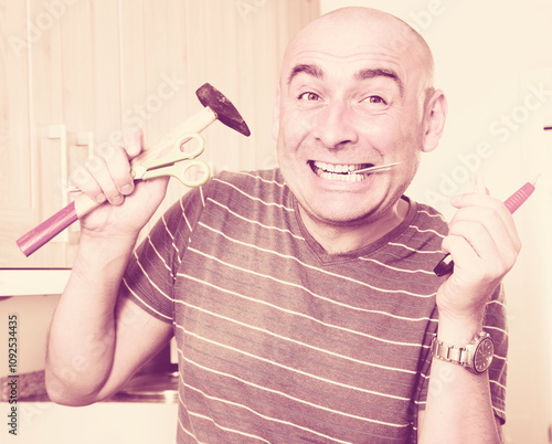 imposing man in prime of life holds in teeth of screws and holding hammer photo