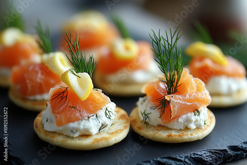 Mini smoked salmon blinis topped with cream cheese, dill, and a tiny lemon twist, arranged on a slate platter photo