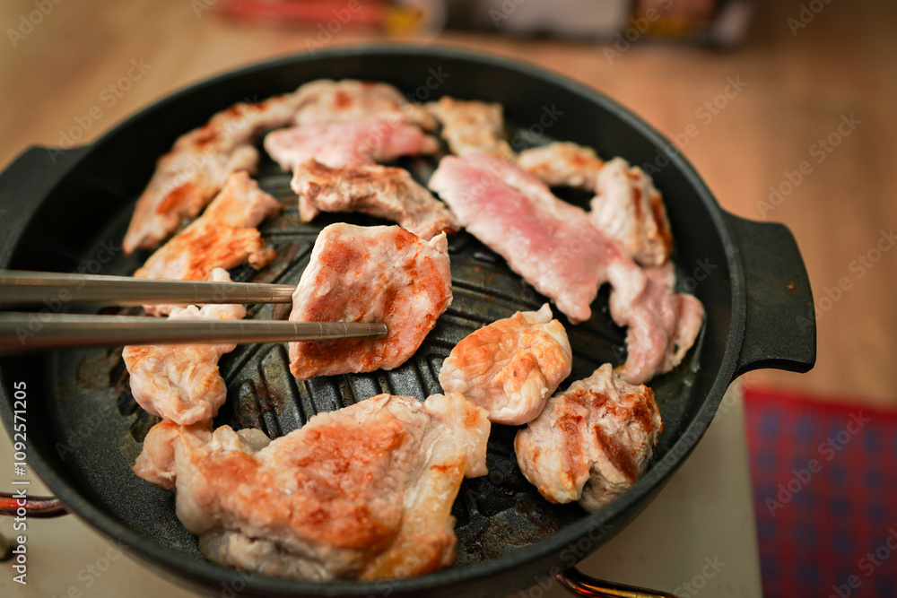 Hand of Using stainless steel chopsticks, there is grilled sliced pork or MOO KA TA, grilled food on a pan, Asian style eating. Hand of Using stainless steel chopsticks, there is grilled sliced pork or MOO KA TA, grilled food on a pan, Asian style eating.