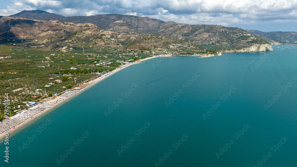 Fototapeta premium Aerial view of the beach of Mattinata, in the province of Foggia, Puglia, Italy. The beach is crowded with many umbrellas and beach clubs on this beautiful sunny summer day. Holidays on Gargano.