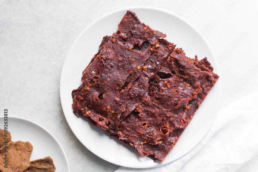 Overhead view of Nigerian kilishi on a white plate, top view of nigerian spicy beef jerky, flatlay of dried beef suya Overhead view of Nigerian kilishi on a white plate, top view of nigerian spicy beef jerky, flatlay of dried beef suya