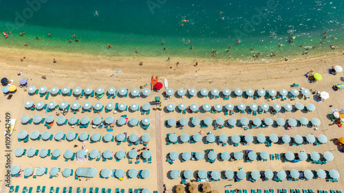 Aerial view of a beach club with blue umbrellas in Puglia, Italy. The beach is sandy and crowded on this beautiful sunny summer day. Vacation on the Mediterranean Sea.