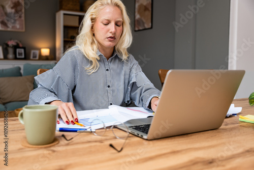 Businesswoman working on laptop computer sitting at home and managing her business via home office during menstruation period. Freelance work female online e-commerce calculating teleworking job.