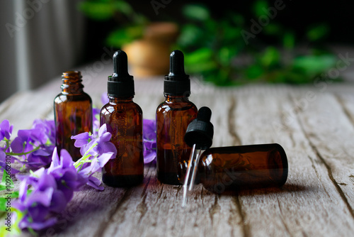 Some amber vials of essential oils with flowers on a wooden surface.