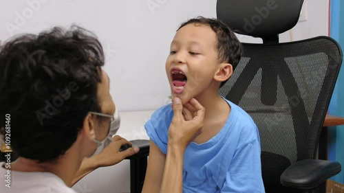 a doctor is diagnosing by checking the open mouth of a young child patient in his room. medical concept