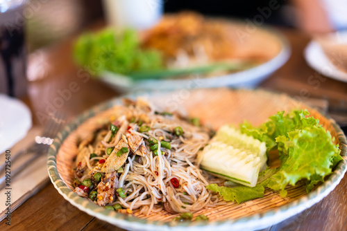 Papaya salad with rice vermicelli on a plate ready to eat on a wooden table in a restaurant photo