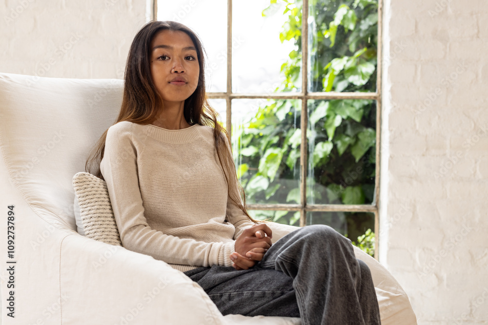 asian female teenager relaxing on cozy chair at home, looking thoughtful by window asian female teenager relaxing on cozy chair at home, looking thoughtful by window