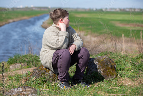 A chubby, plump teenage boy of twelve years old sits against the backdrop of nature and is sad. photo