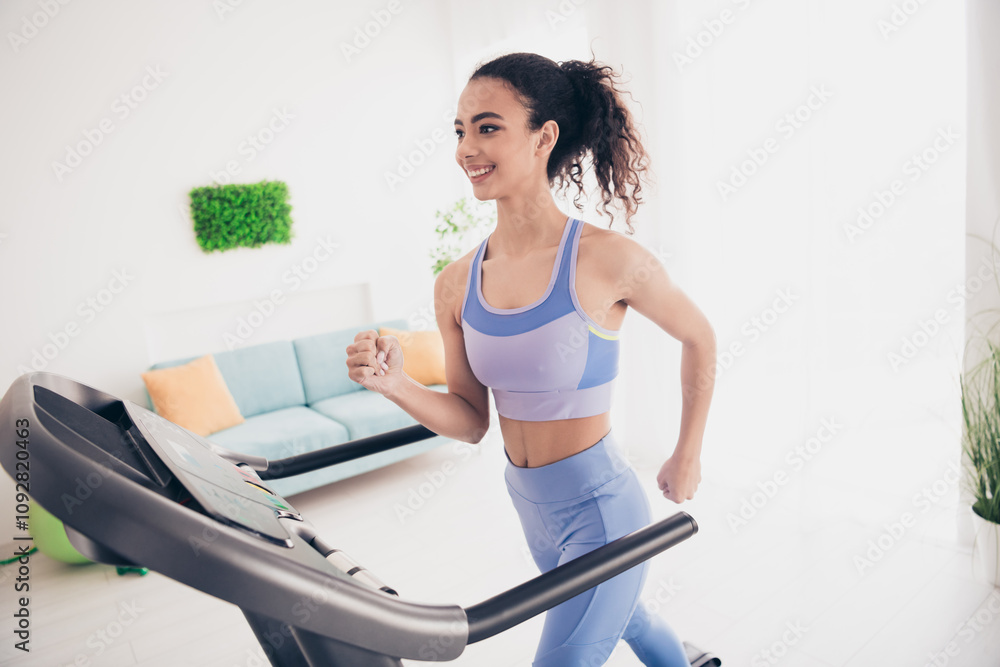 Fototapeta premium Energetic woman in stylish activewear enjoys treadmill workout in bright modern home interior
