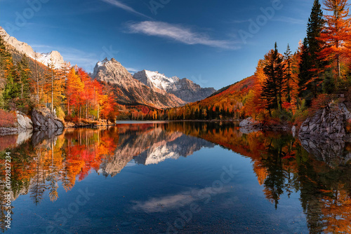 A serene lake reflects colorful autumn trees and mountains, with bright red, orange, and yellow foliage creating a picturesque scene, ai.