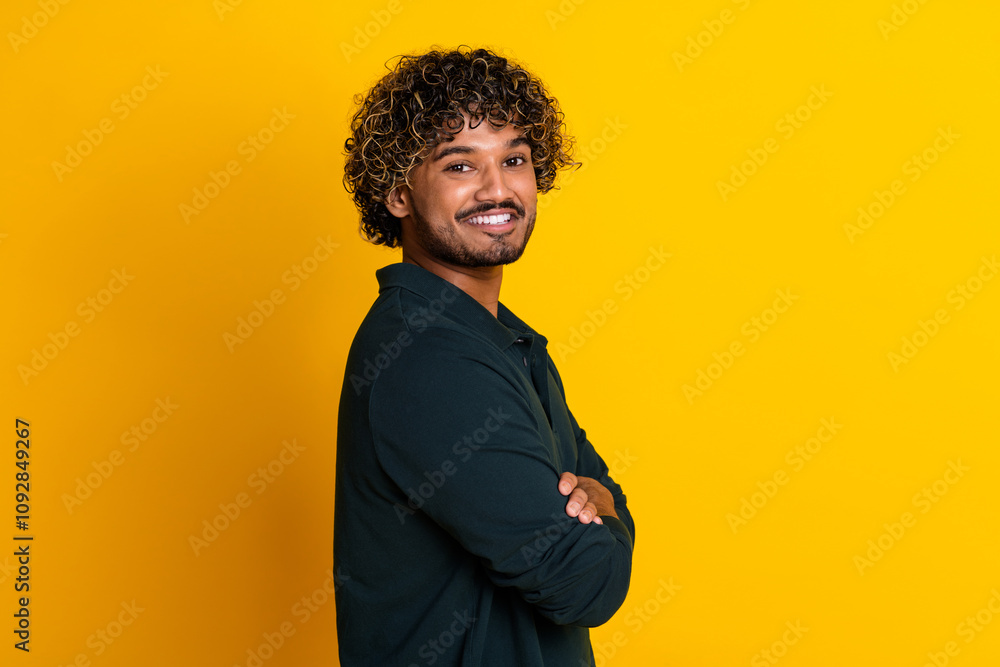 Confident young man in black shirt posing with crossed arms against vibrant yellow background Confident young man in black shirt posing with crossed arms against vibrant yellow background