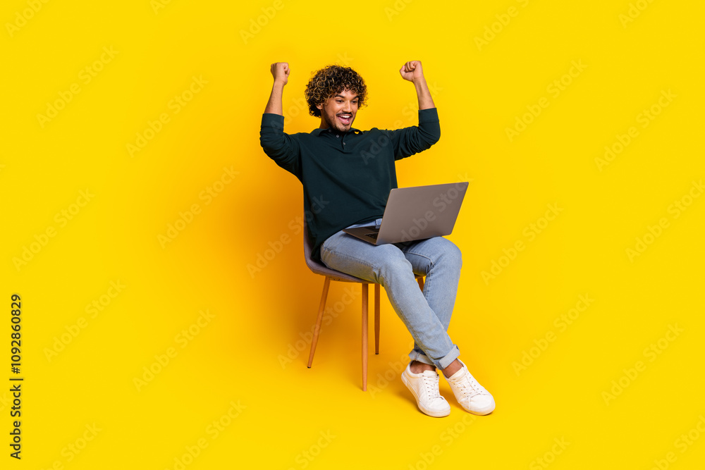 Joyful young man celebrating online success while using laptop in vibrant yellow setting Joyful young man celebrating online success while using laptop in vibrant yellow setting