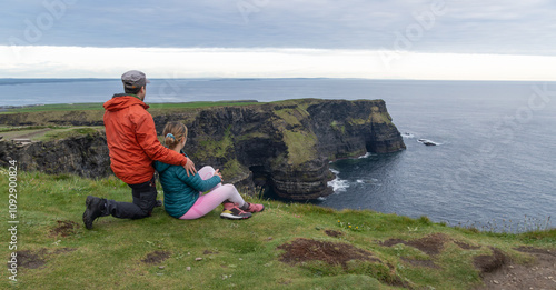 Couple sitting looking at the landscape of the cliffs of moher ireland. couple of tourists hiking enjoying the tranquility of the landscape.