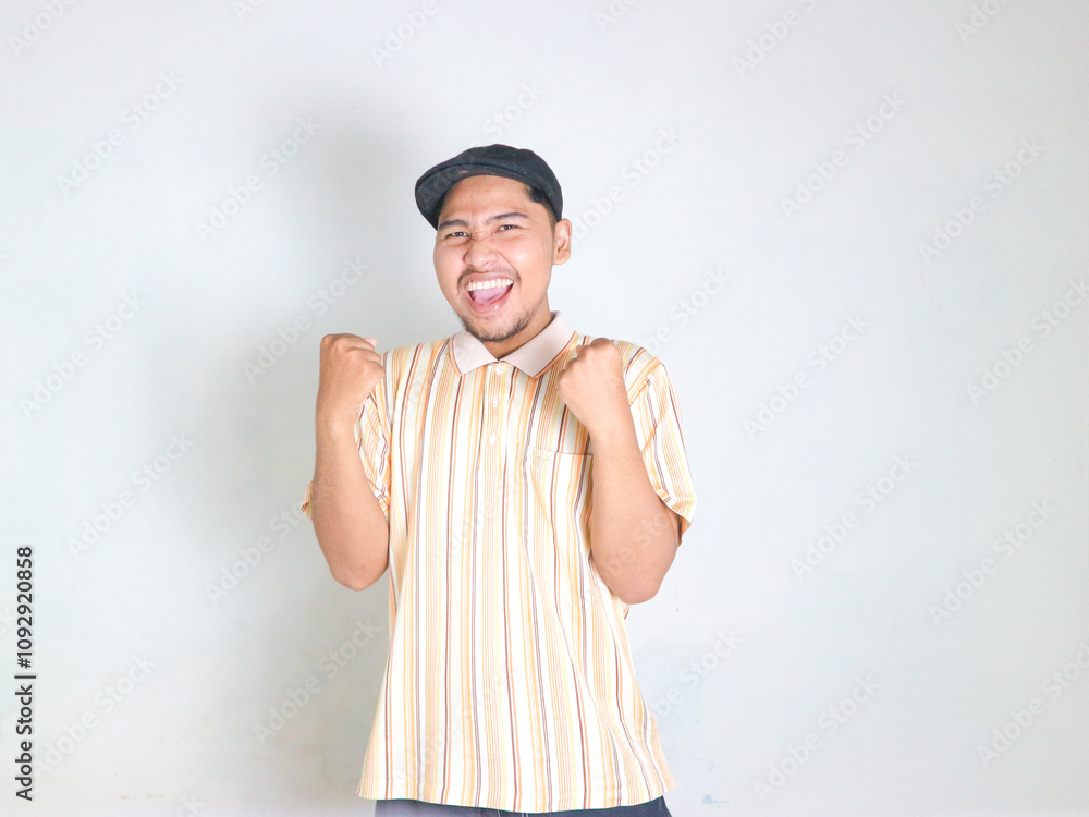 young asian man wearing striped polo shirt celebrating victory and rejoicing because he has achieved success while shouting and raising his hands young asian man wearing striped polo shirt celebrating victory and rejoicing because he has achieved success while shouting and raising his hands