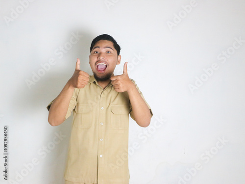 Asian male Indonesian civil servant wearing a brown uniform commonly called keki smiles and gives a thumbs up. OK gesture. Indonesian civil servants, ASN photo