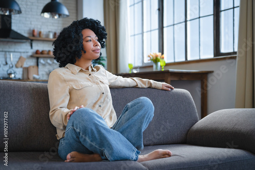 Foto Young calm black woman relaxing sit on comfortable sofa in modern living room, l