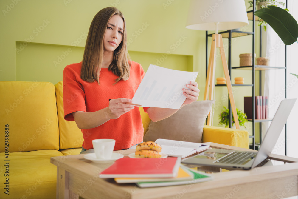 Photo of lovely young girl skeptical working papers dressed orange garment spacious house spring indoors room Photo of lovely young girl skeptical working papers dressed orange garment spacious house spring indoors room