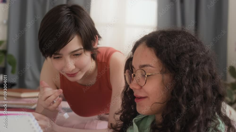 Close-up shot of two teenage girls studying together in cozy bedroom, discussing their homework intently Close-up shot of two teenage girls studying together in cozy bedroom, discussing their homework intently
