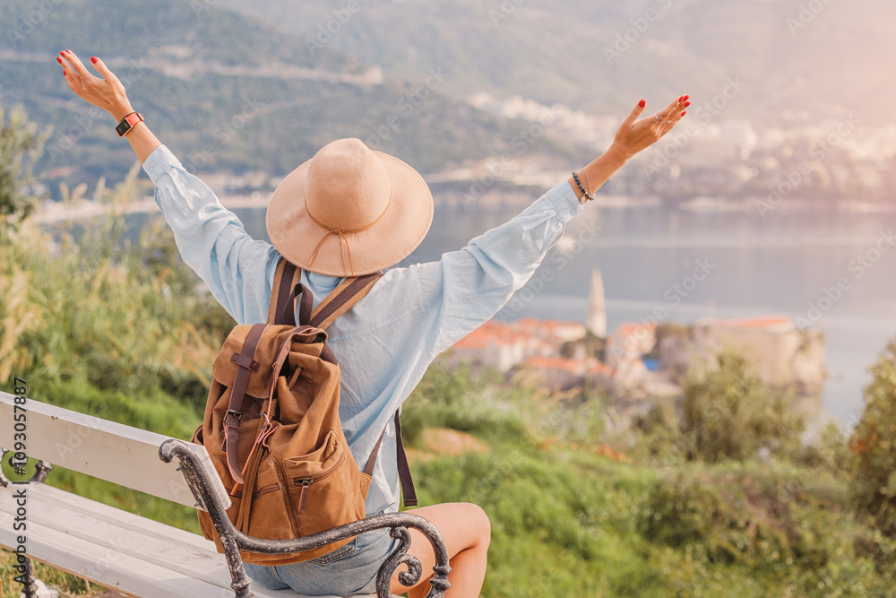 Female tourist with backpack sitting on bench and raising arms, enjoying beautiful view of Budva in Montenegro