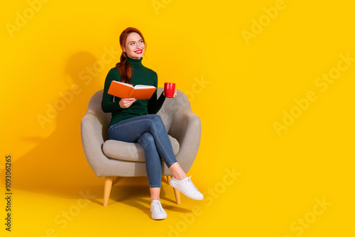 Full length photo of adorable lovely girl wear green pullover sitting sofa enjoy book drink tel look empty space isolated yellow color background