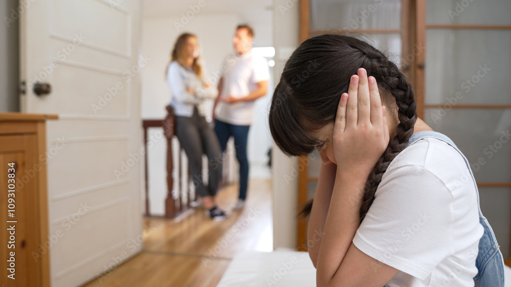 Fototapeta premium Stressed and unhappy young girl huddle in corner, cover her ears blocking sound of her parent arguing in background. Domestic violence at home and traumatic childhood develop to depression. Synchronos