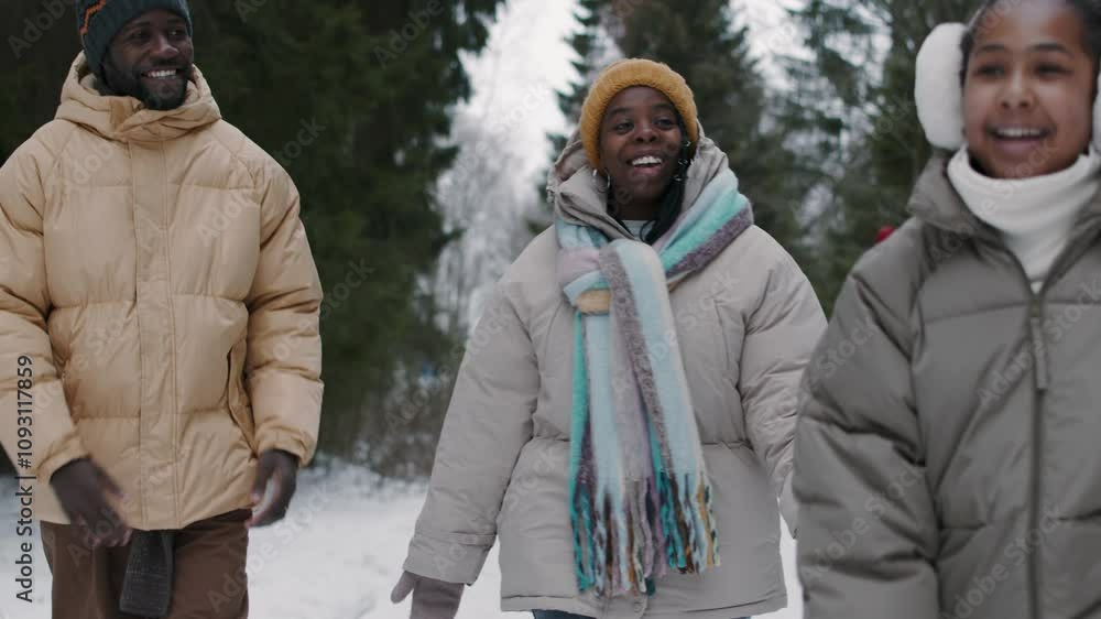 Happy teen girl running between positive Black young parents in winter forest, then they walking together and embracing Happy teen girl running between positive Black young parents in winter forest, then they walking together and embracing