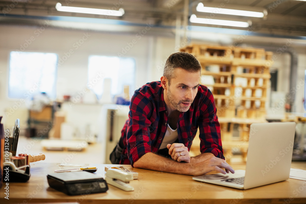 Young man using a laptop while working in a printing press office Young man using a laptop while working in a printing press office