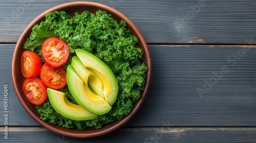 A vibrant bowl of fresh kale topped with sliced avocado and cherry tomatoes, showcasing healthy, colorful ingredients on a rustic wooden surface.