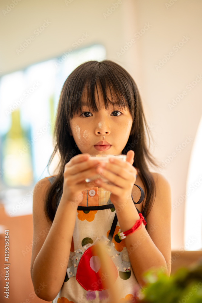 Asian girl drinking milk from a glass in kitchen Asian girl drinking milk from a glass in kitchen