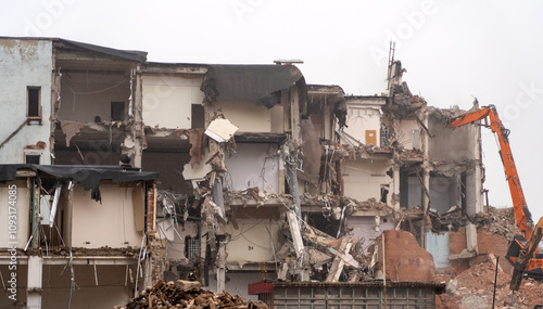 Ongoing demolition work exposes the wreckage of a dilapidated structure, showcasing heavy machinery against a gray sky and scattered debris photo