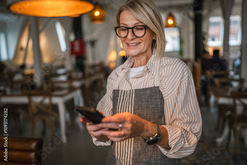 mature woman waitress in apron stand at restaurant and use cellphone