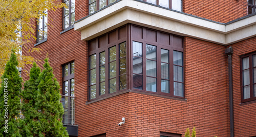 A contemporary brick building features expansive windows, nestled among lush greenery in a peaceful residential area during daylight