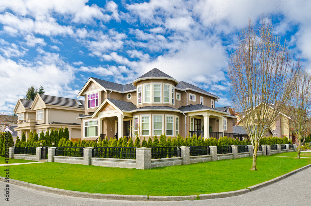 Fototapeta premium Neighbourhood of luxury houses in summer with street road, big trees and nice landscape in Vancouver, Canada. Blue sky. Day time on August 2024.