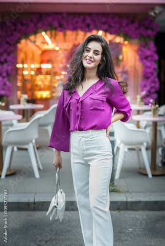Obraz na płótnie Young beautiful brunette woman in a pink jacket and white pants posing on the street. Portrait of a beautiful young woman in a purple blouse and white pants posing in an outdoor cafe on the street w salonie