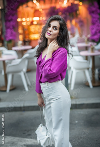 Obraz na płótnie Young beautiful brunette woman in a pink jacket and white pants posing on the street. Portrait of a beautiful young woman in a purple blouse and white pants posing in an outdoor cafe on the street w salonie