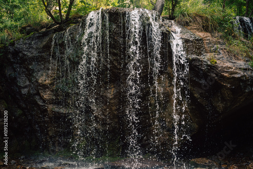 Close-up of a small waterfall flowing over a rocky cliff surrounded by lush greenery