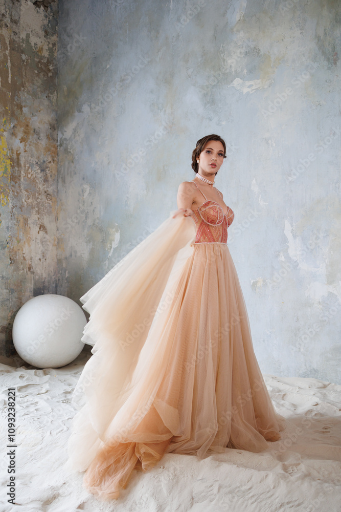 A beautiful girl in a long elegant beige gold wedding dress stands on the sand. Portrait of a beautiful bride on a gray background. Bright make-up and bundle styling. Gorgeous brunette woman A beautiful girl in a long elegant beige gold wedding dress stands on the sand. Portrait of a beautiful bride on a gray background. Bright make-up and bundle styling. Gorgeous brunette woman