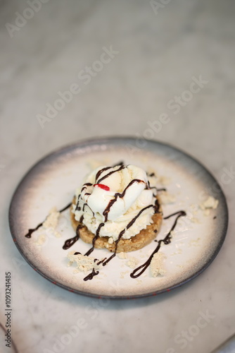 Delicious ice cream served on a crumbly cookie base, drizzled with chocolate syrup and topped with a cherry, presented on a stylish ceramic plate.
