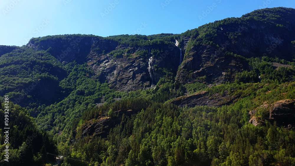 Majestic Mountain Landscape with Dense Forests and Cascading Waterfalls Under a Clear Blue Sky Majestic Mountain Landscape with Dense Forests and Cascading Waterfalls Under a Clear Blue Sky
