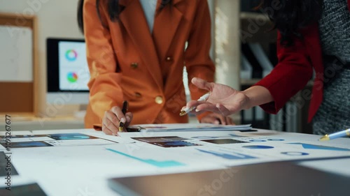 Businesswomen collaborating in a working session, analyzing marketing data on paper documents in a corporate office setting