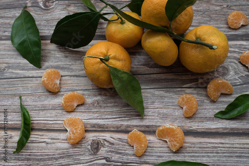 segments of tangerine and tangerines with leaves on a wooden table photo