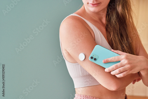 Young girl with diabetes uses smart remote sensor and smartphone for controlling and monitoring of blood sugar level at home, modern active diabetic lifestyle
