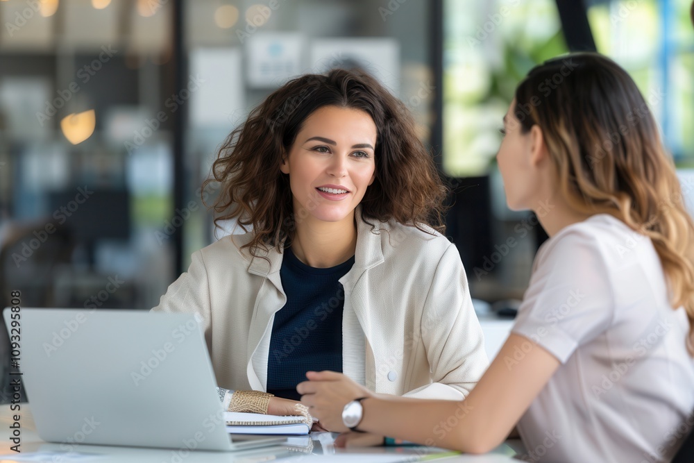 Two professional women engaging in a discussion at a desk, with a laptop and documents, in a bright, modern office environment. Two professional women engaging in a discussion at a desk, with a laptop and documents, in a bright, modern office environment.