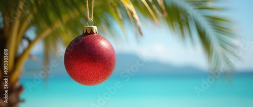 Red Christmas ornament hanging from palm tree branch, with turquoise ocean in background. Tropical, beach, holiday themes, background with copy space photo