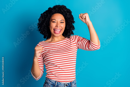 Photo of nice young woman raise fists triumph wear striped shirt isolated on blue color background