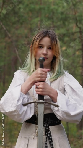 blonde young woman in forest plunges sword into ground, tolkienists photo