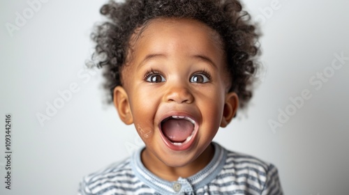 A young child with dark skin and curly hair wearing a striped shirt opens their mouth in a joyful expression.